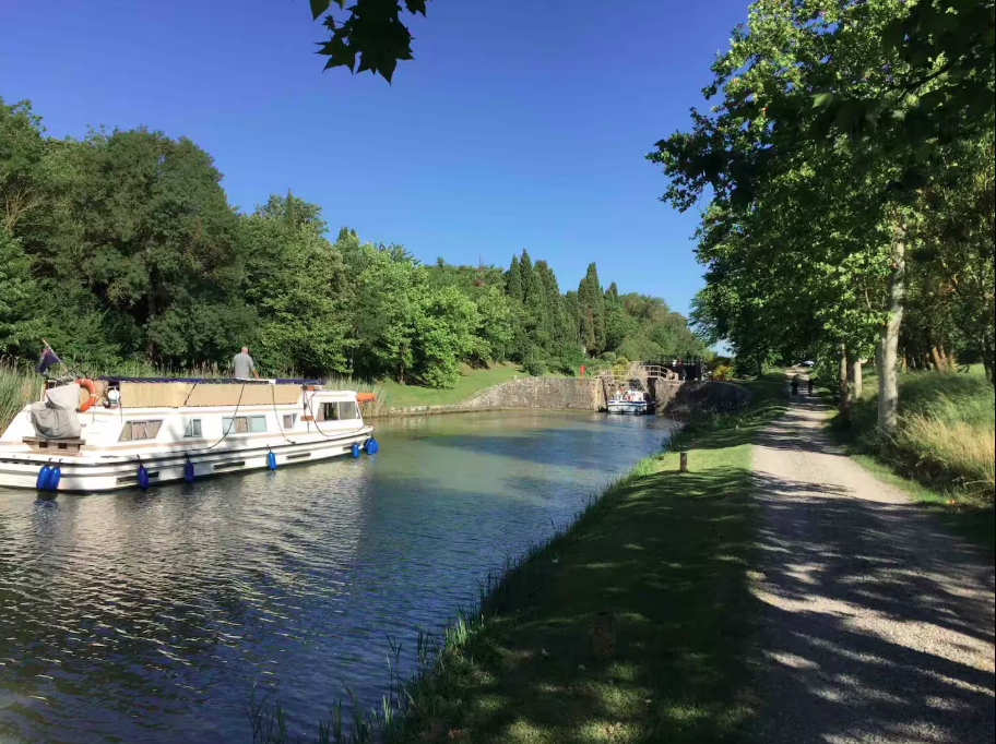 A row of boats are docked on a river next to a path.