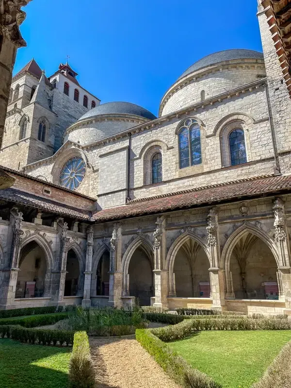 Stone cloister courtyard with arches and domed church under a bright blue sky