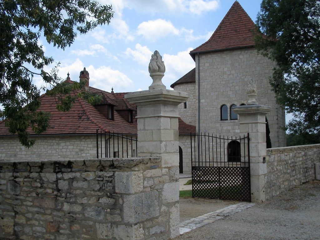 Stone gate and courtyard entrance to a small building with red roofs and a statue on top, under a blue sky