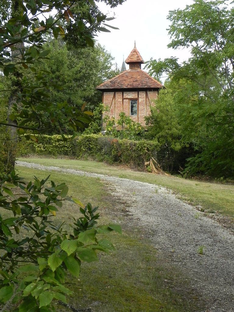 Stone tower with a conical roof beside a gravel path, surrounded by dense green trees.