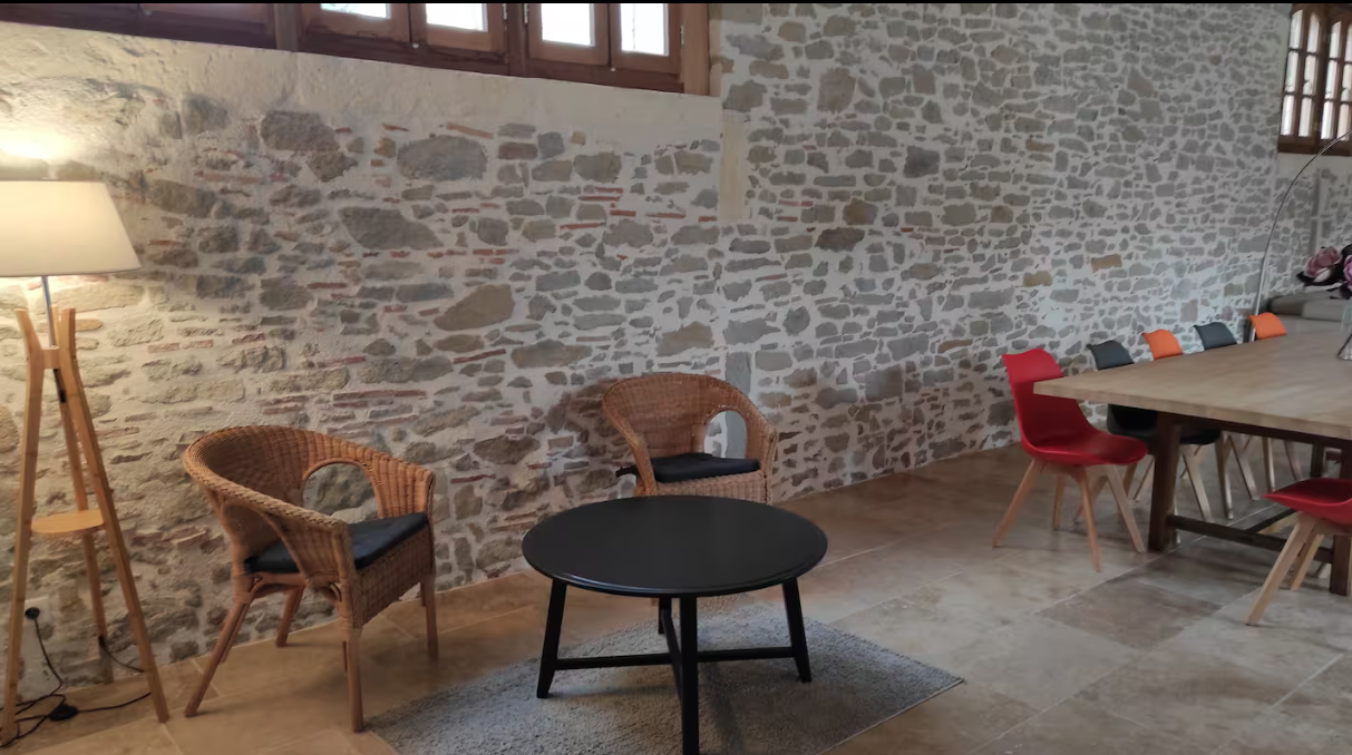 A room with a table and chairs in front of a stone wall.