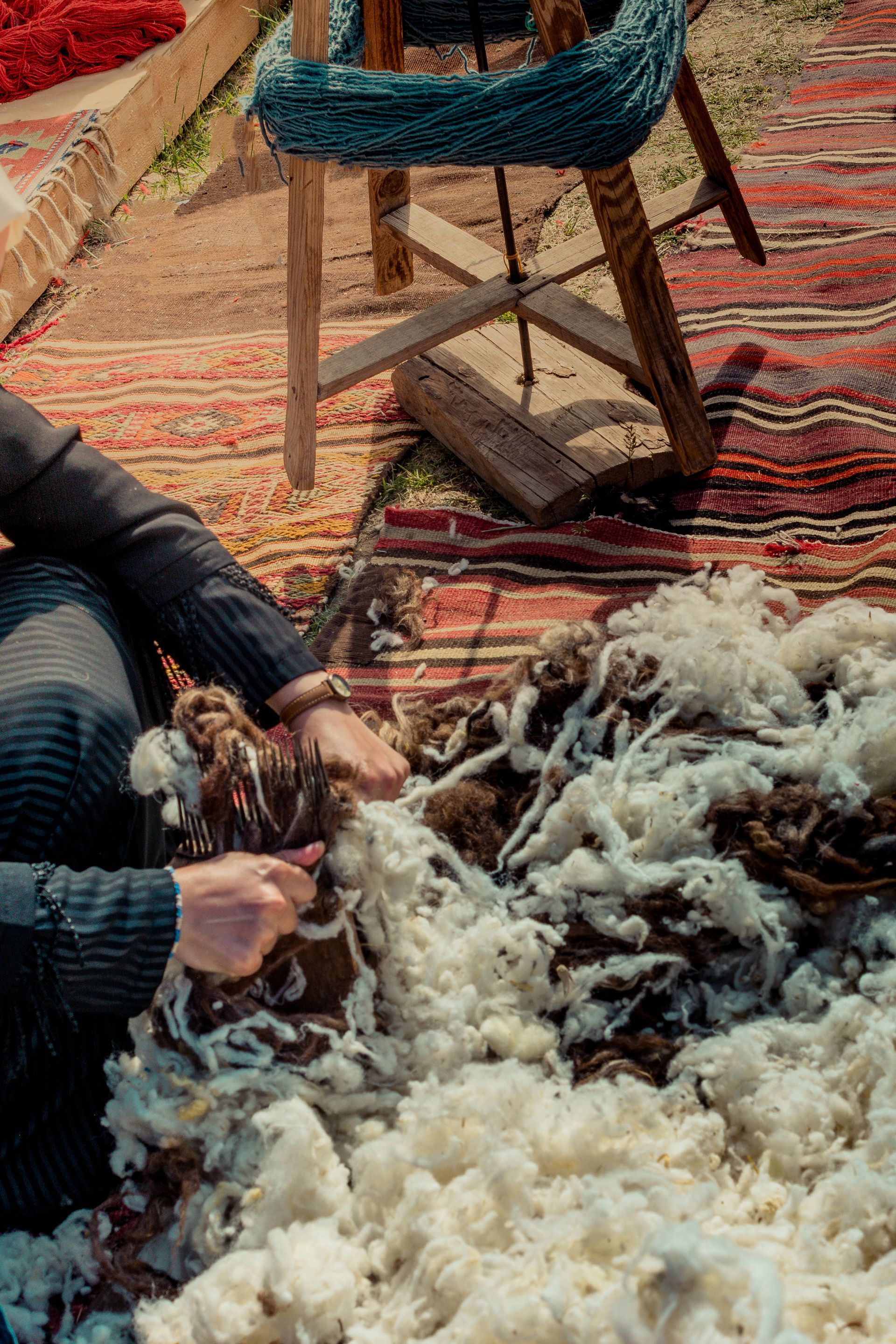 A person is sitting on a rug cutting wool.