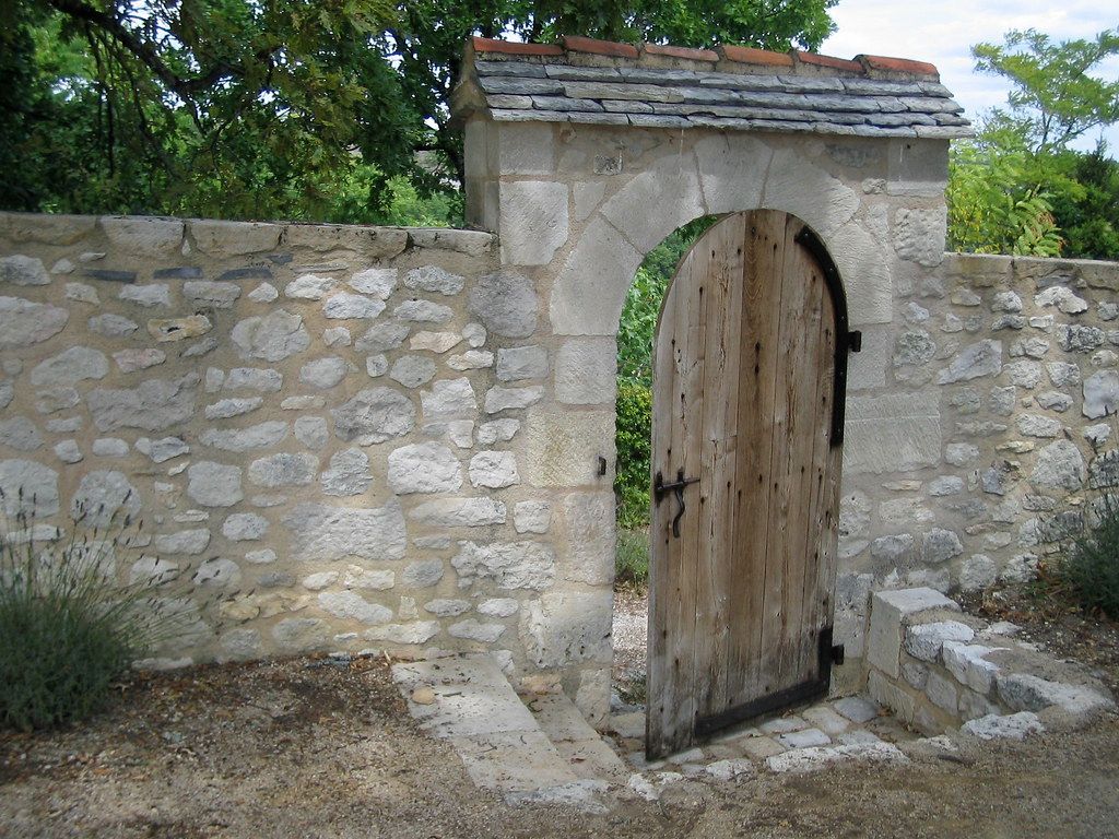 Stone wall with an open wooden gate and arched doorway in a garden setting