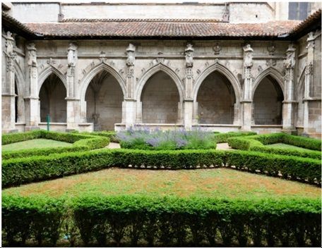 Stone cloister courtyard with Gothic arches and a manicured green hedge garden