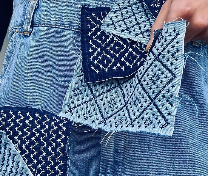 Patchwork denim jeans with blue patterned fabric panels and frayed edges