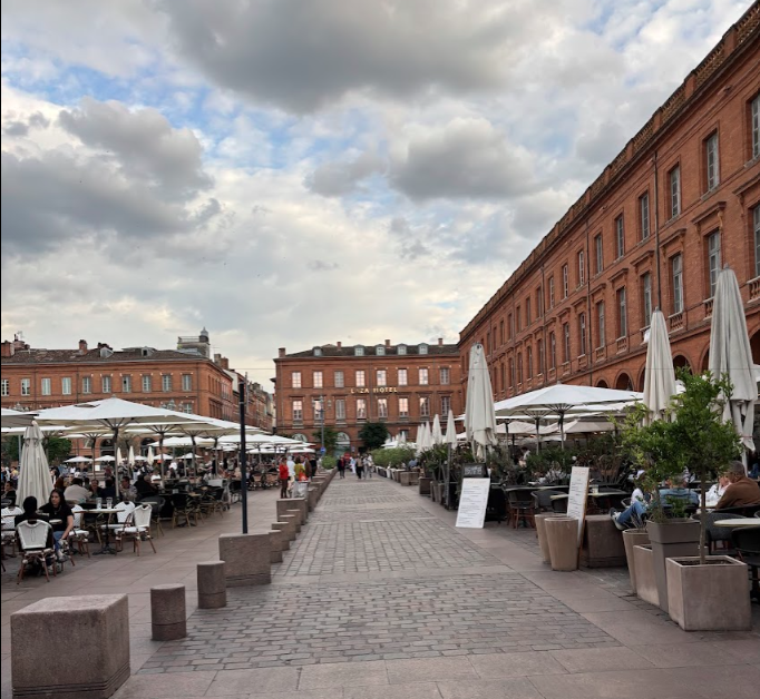 A row of tables with umbrellas in front of a building in the Toulouse square, Fleur de Lys Retreats.