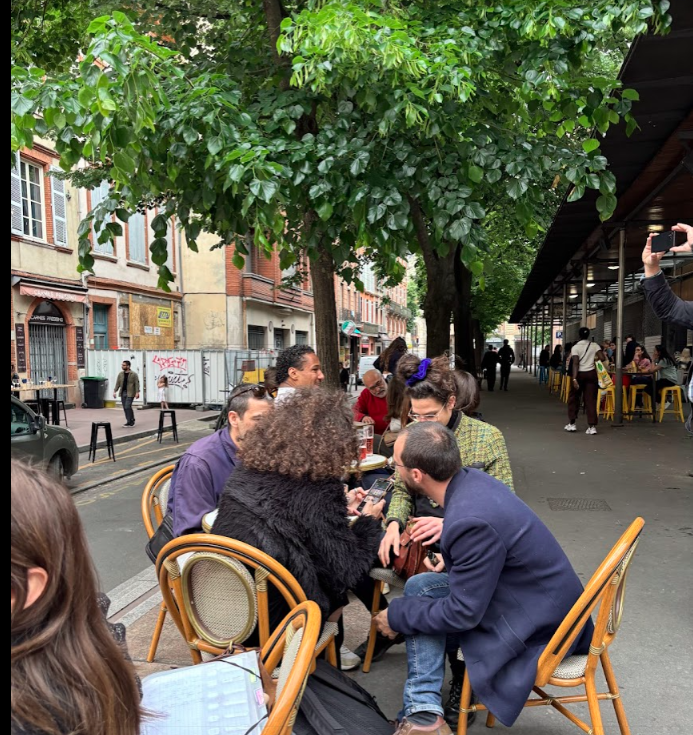 A man is taking a picture of a group of people sitting at tables outside in Toulouse, Fleur de Lys Retreats.