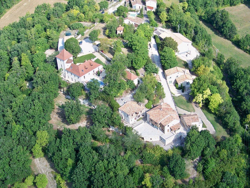 Aerial view of a small village with white-roofed houses surrounded by dense green forest.