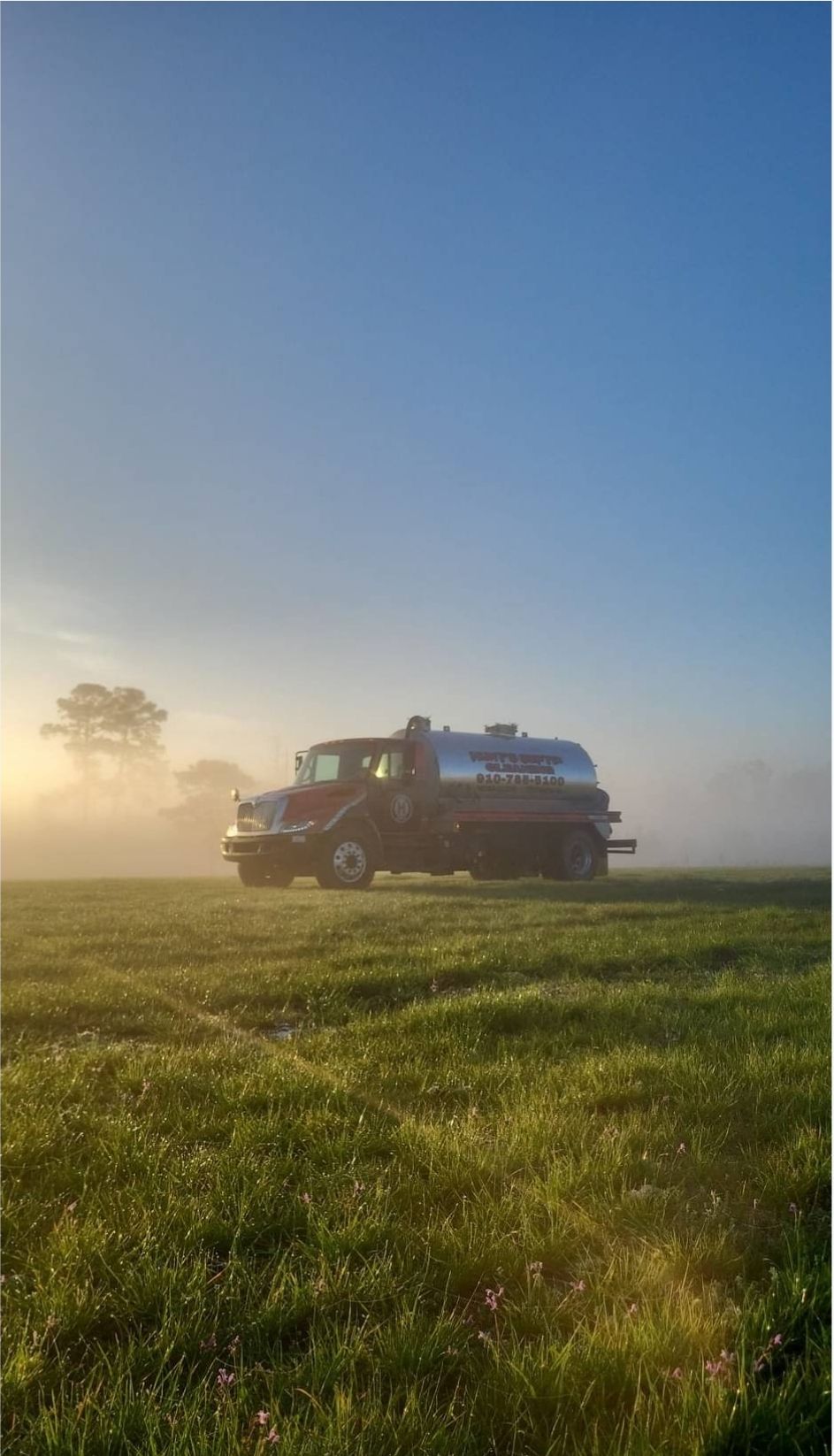 A truck is parked in a grassy field on a foggy day.