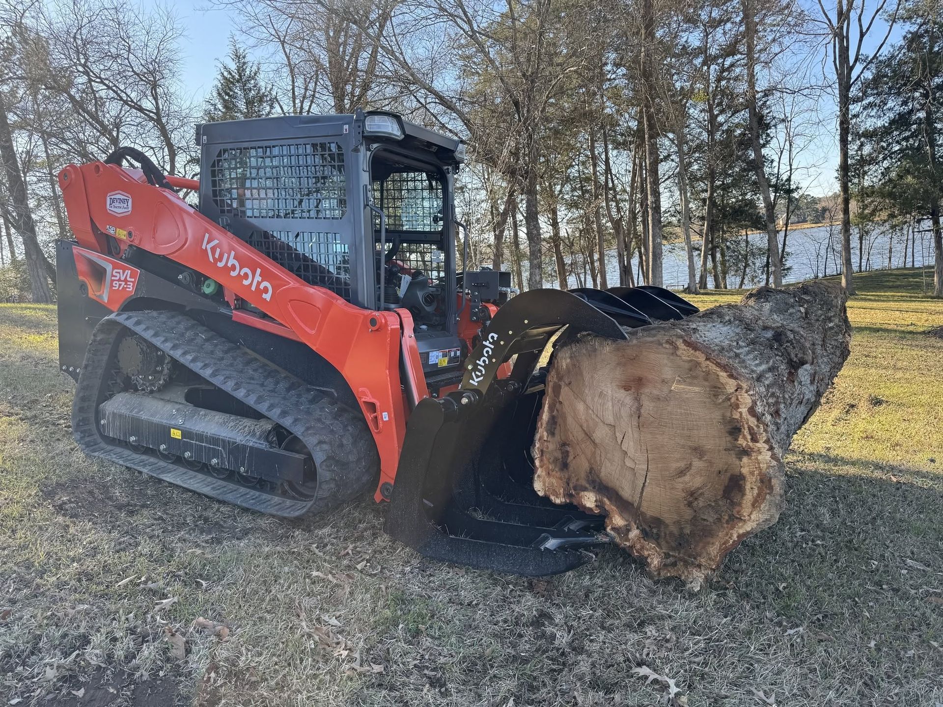 Orange Bobcat skid steer moving a large tree stump in a wooded area