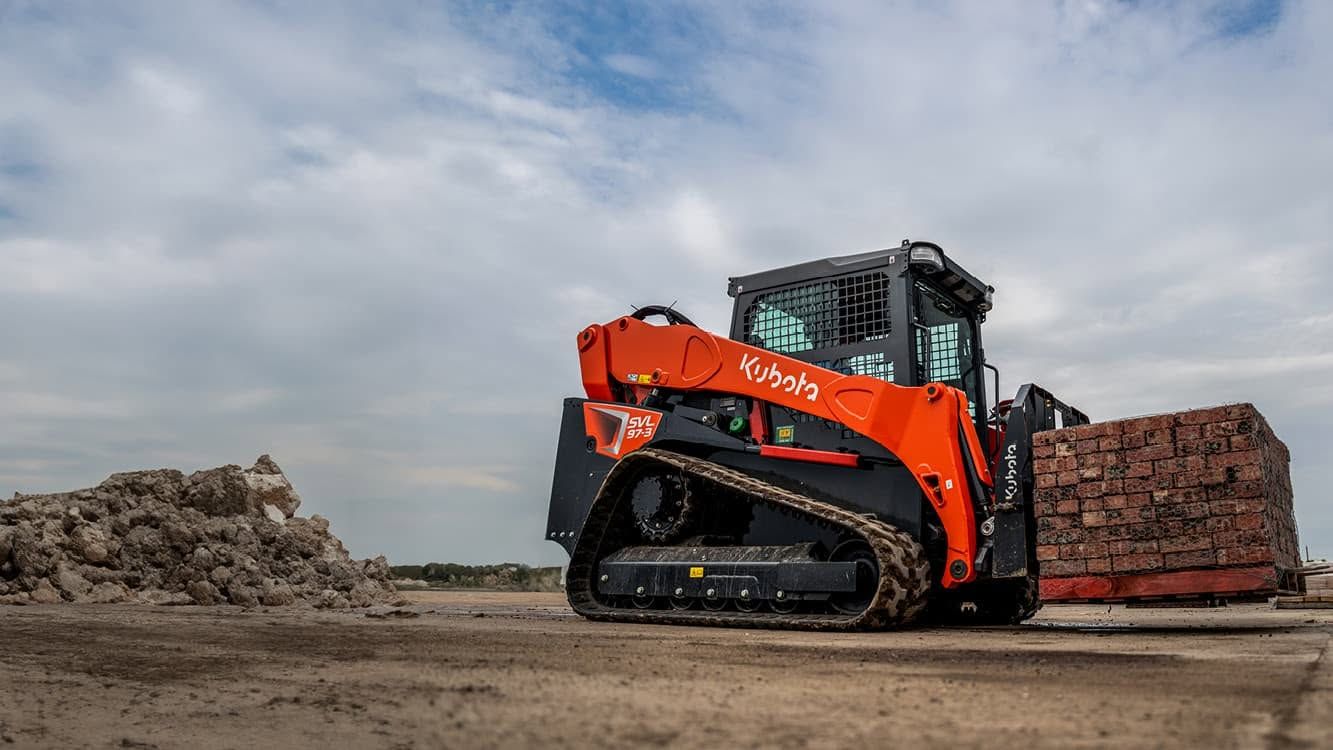 Orange skid-steer loader lifting rubble beside a dirt mound under a cloudy sky