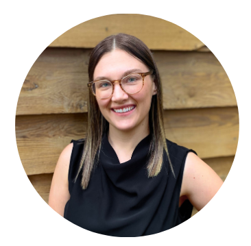 A woman wearing glasses and a black shirt is smiling in front of a wooden wall.