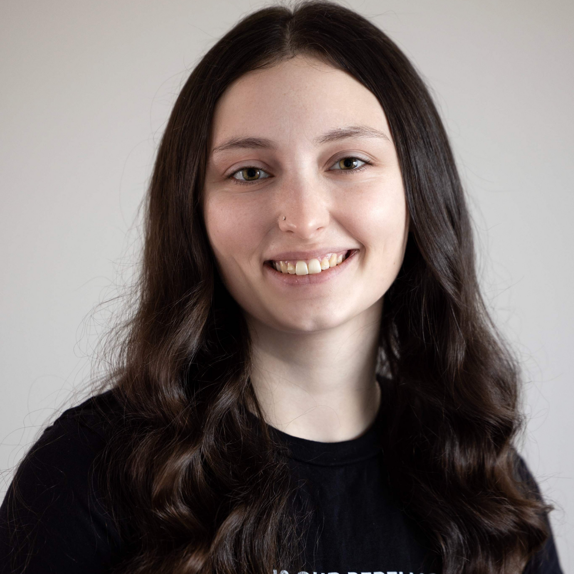 A woman with long brown hair is smiling for the camera while wearing a black shirt.