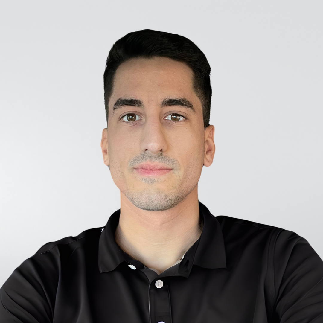 A person with dark hair wearing a black polo shirt against a plain, light gray background.
