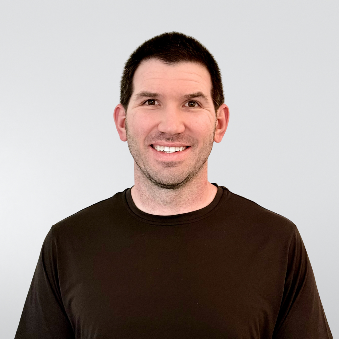 Smiling man in a dark brown shirt against a light gray background