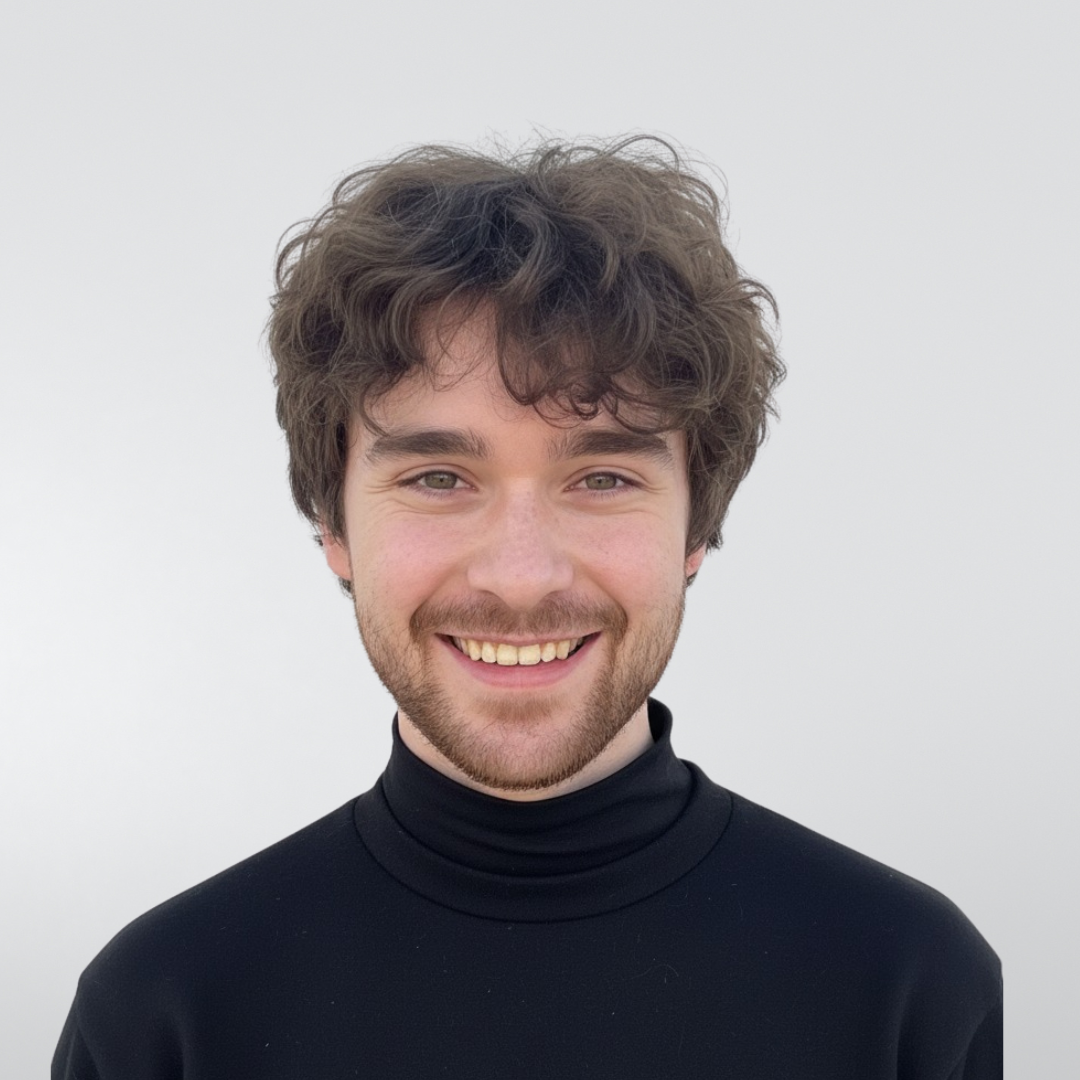 A smiling person with curly dark hair wearing a black turtleneck against a light grey background.