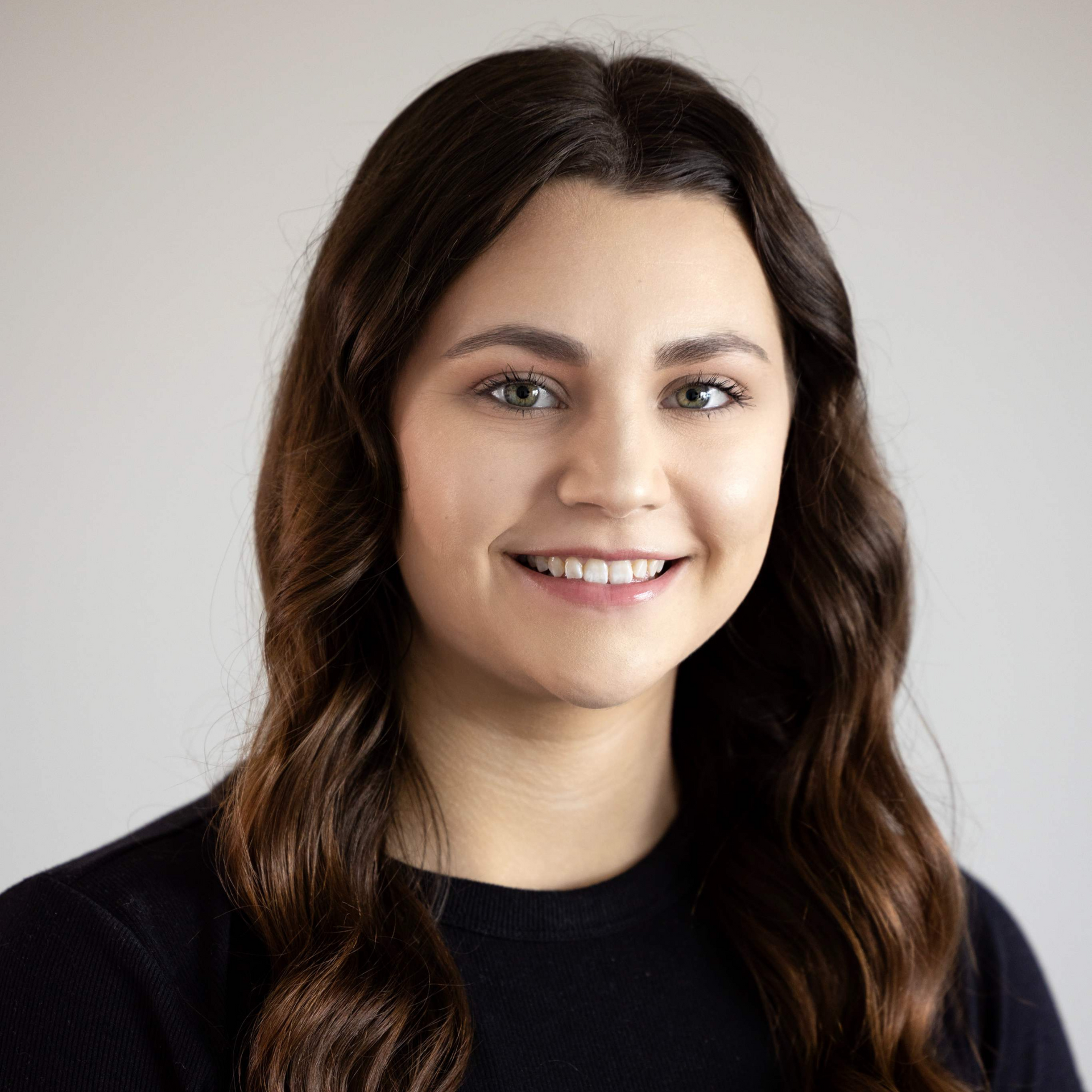 Smiling woman with long dark hair wearing a black top against a light background