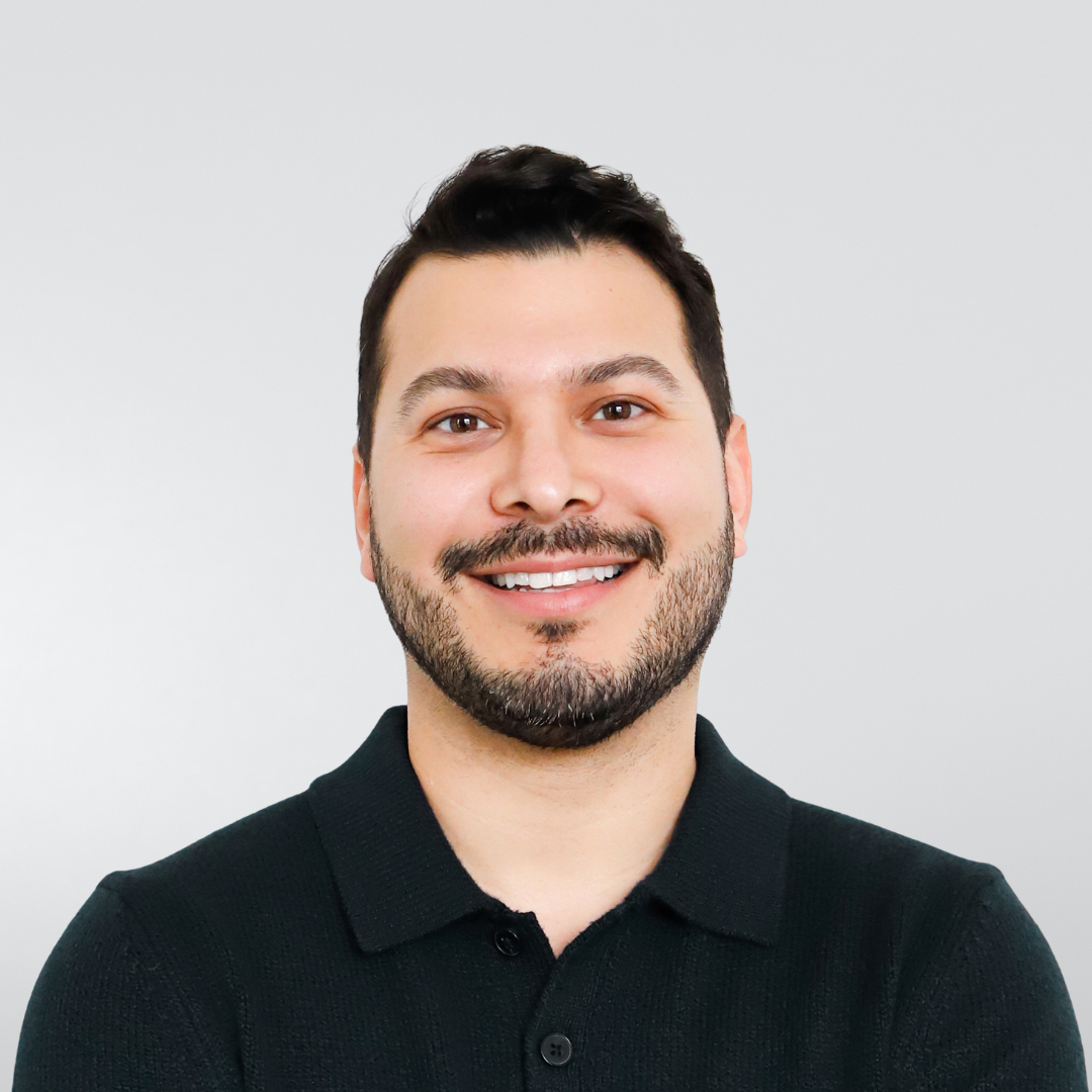 A smiling person with short dark hair and a beard, wearing a dark polo shirt against a light gray background.