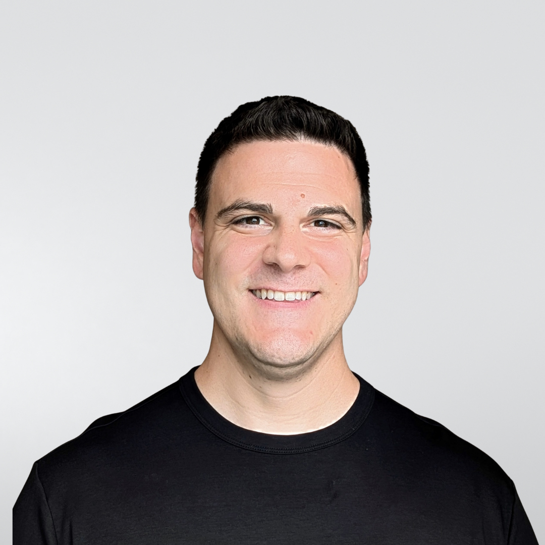 A smiling person wearing a black crew-neck shirt against a plain, light gray background.