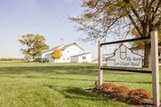 A white barn sits on a grassy field behind a sign that reads, 