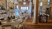 A rustic venue set for a wedding reception with round and long tables decorated with tablecloths and floral centerpieces.