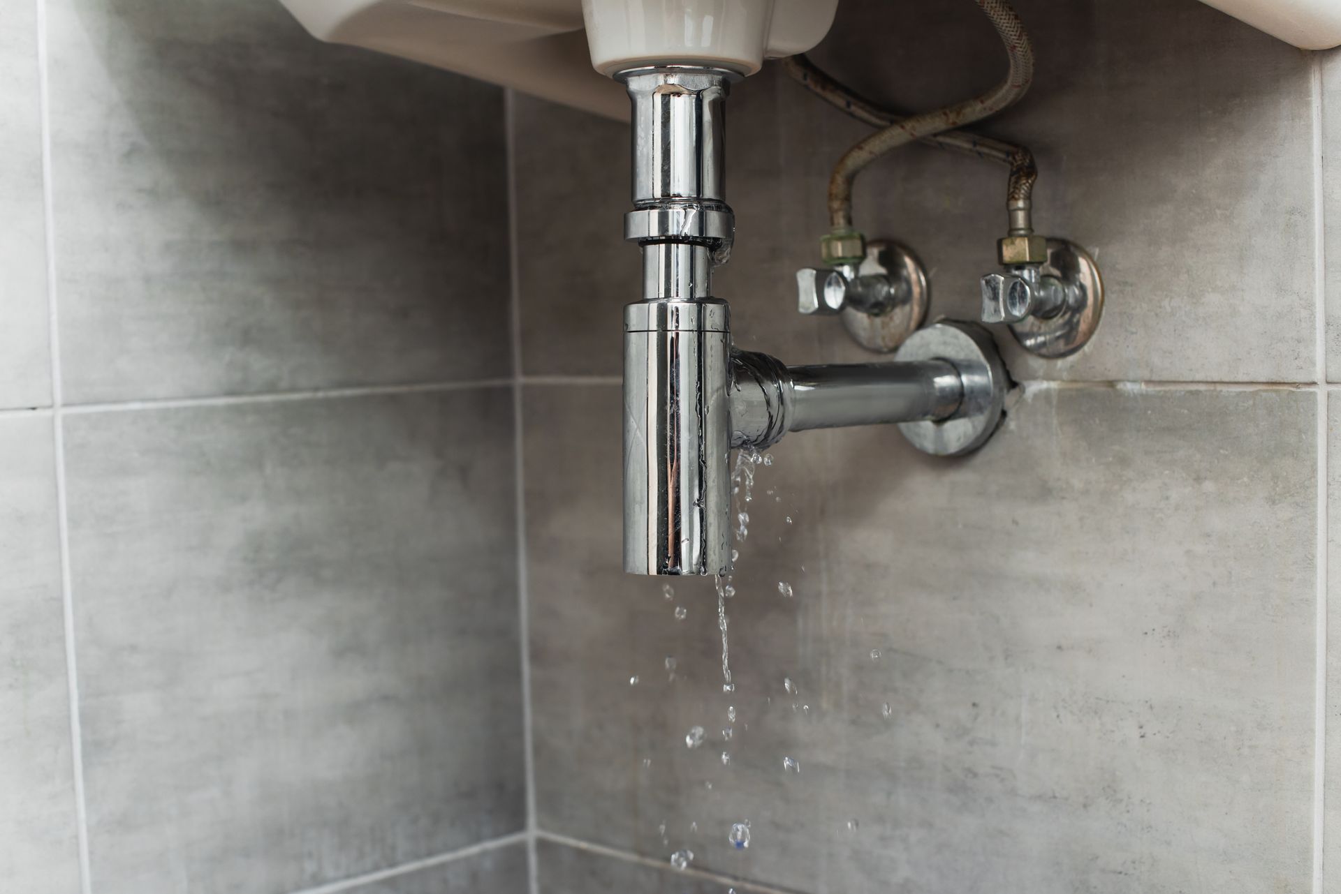 Close-up of steel pipes with a water leak in a bathroom under the sink.