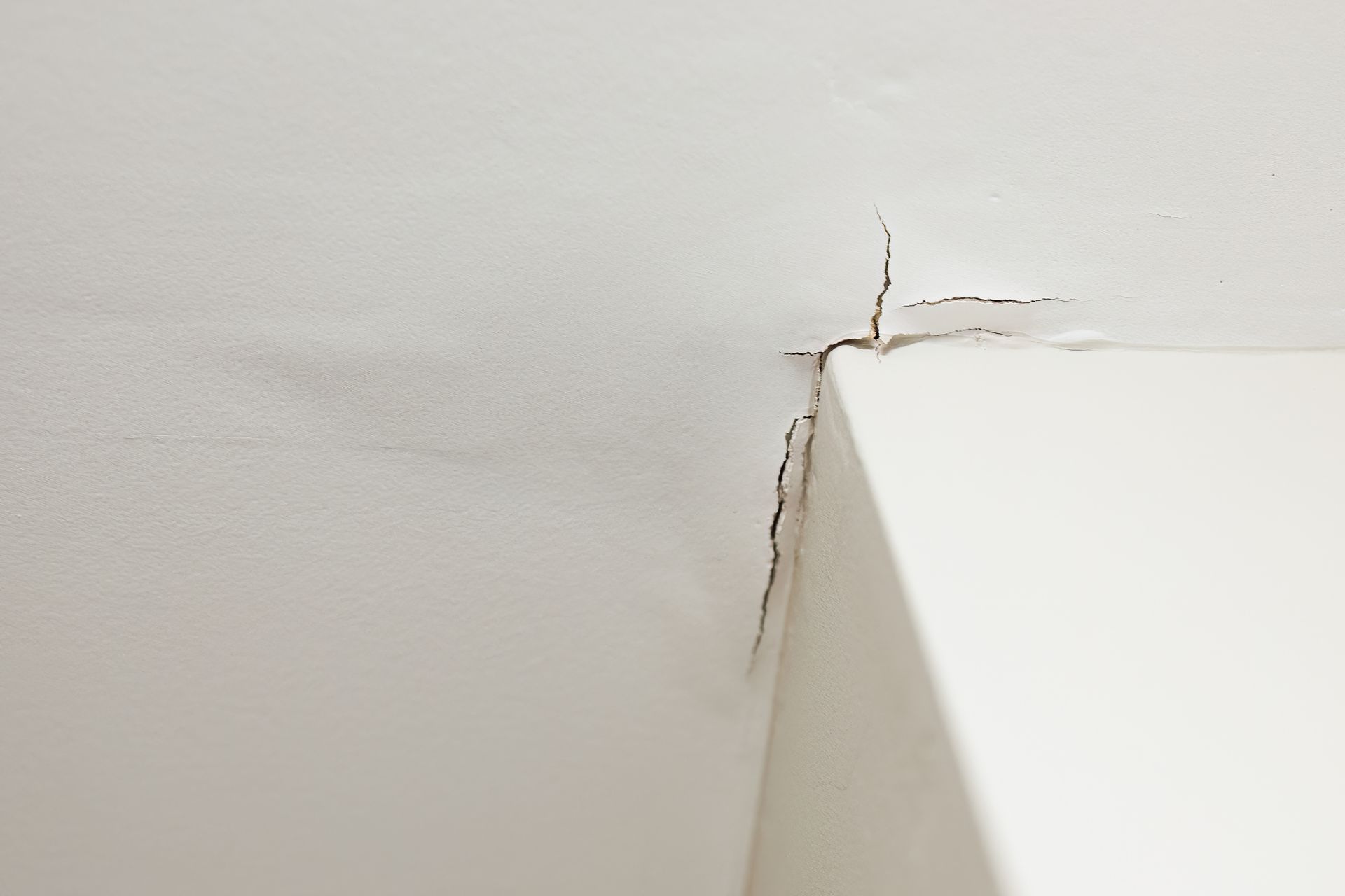 Ceiling corner with cracks and water stains showing signs of a hidden leak and moisture damage.