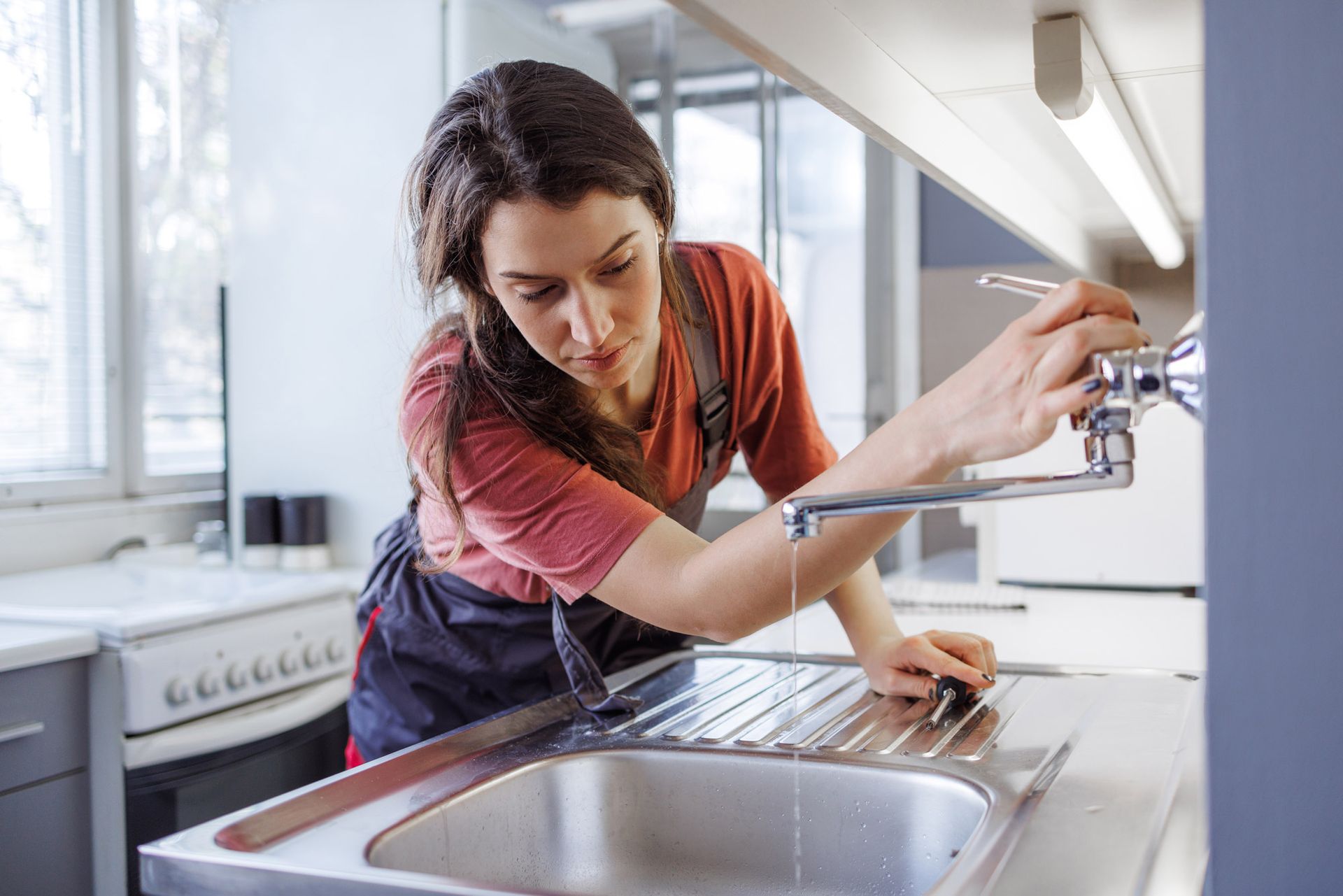 A female plumber works to restore the functionality of the sink and faucet A female plumber works to restore the functionality of the sink and faucet