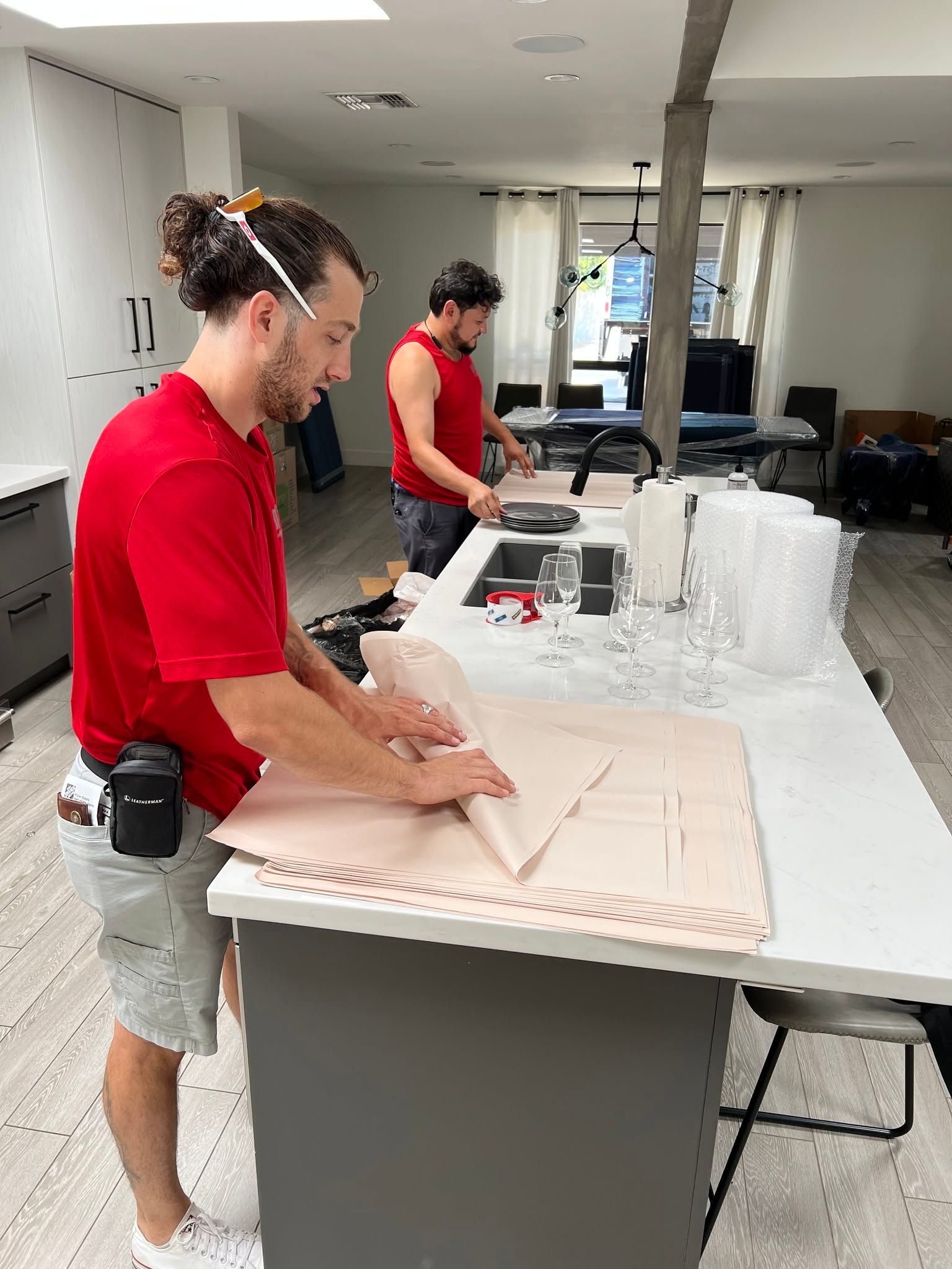 Two people in red shirts working at a table with large sheets and tools in a workshop.
