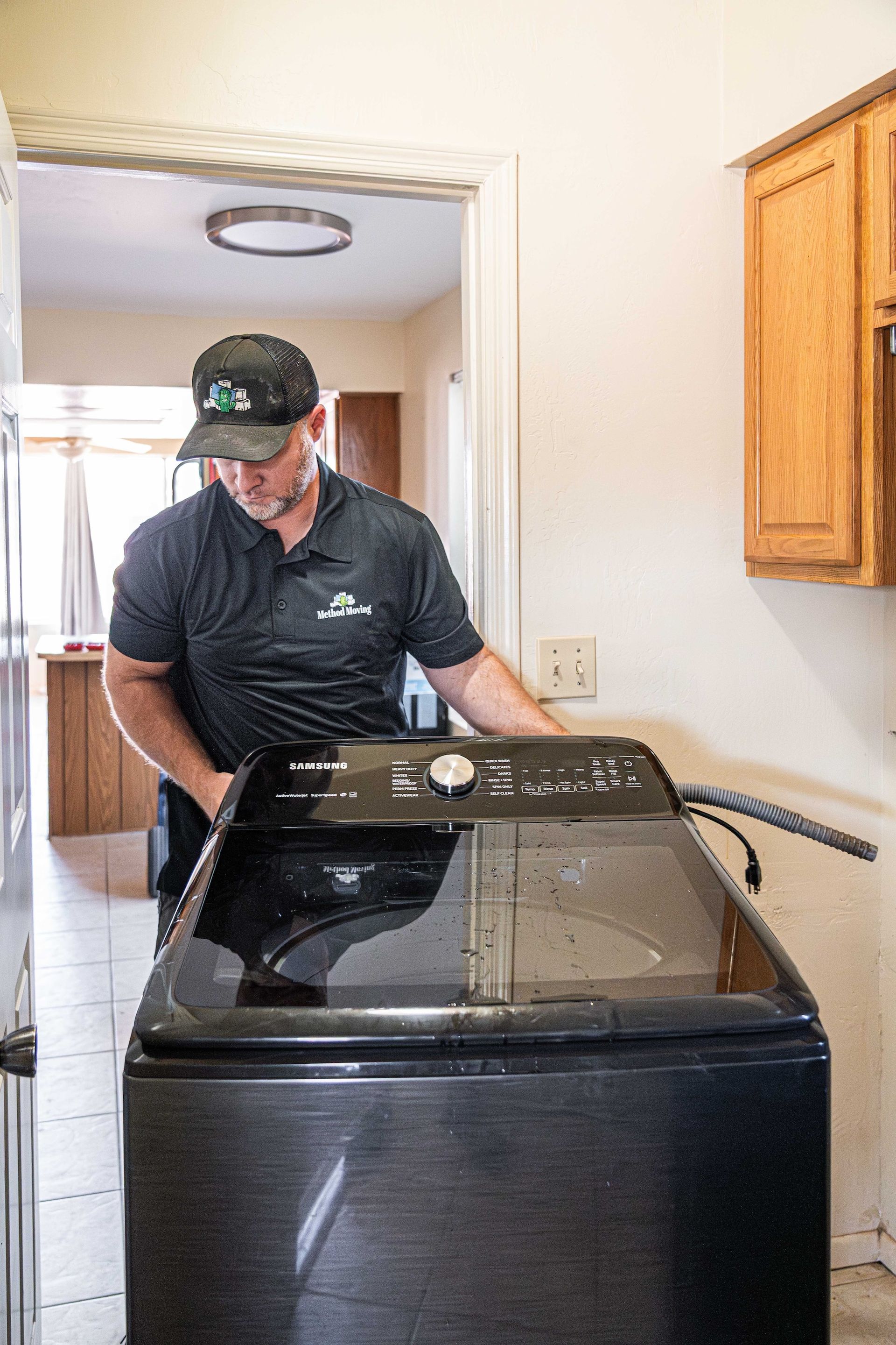 Man standing beside a top-loading washing machine in a laundry room, reaching inside.