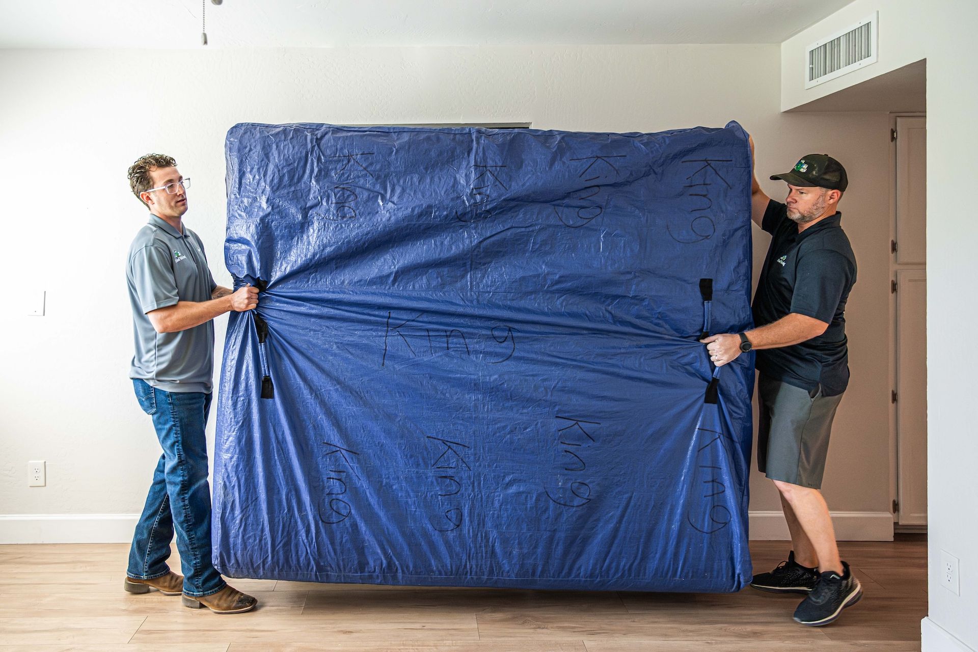 Two men carrying a large blue plastic-wrapped item through a room