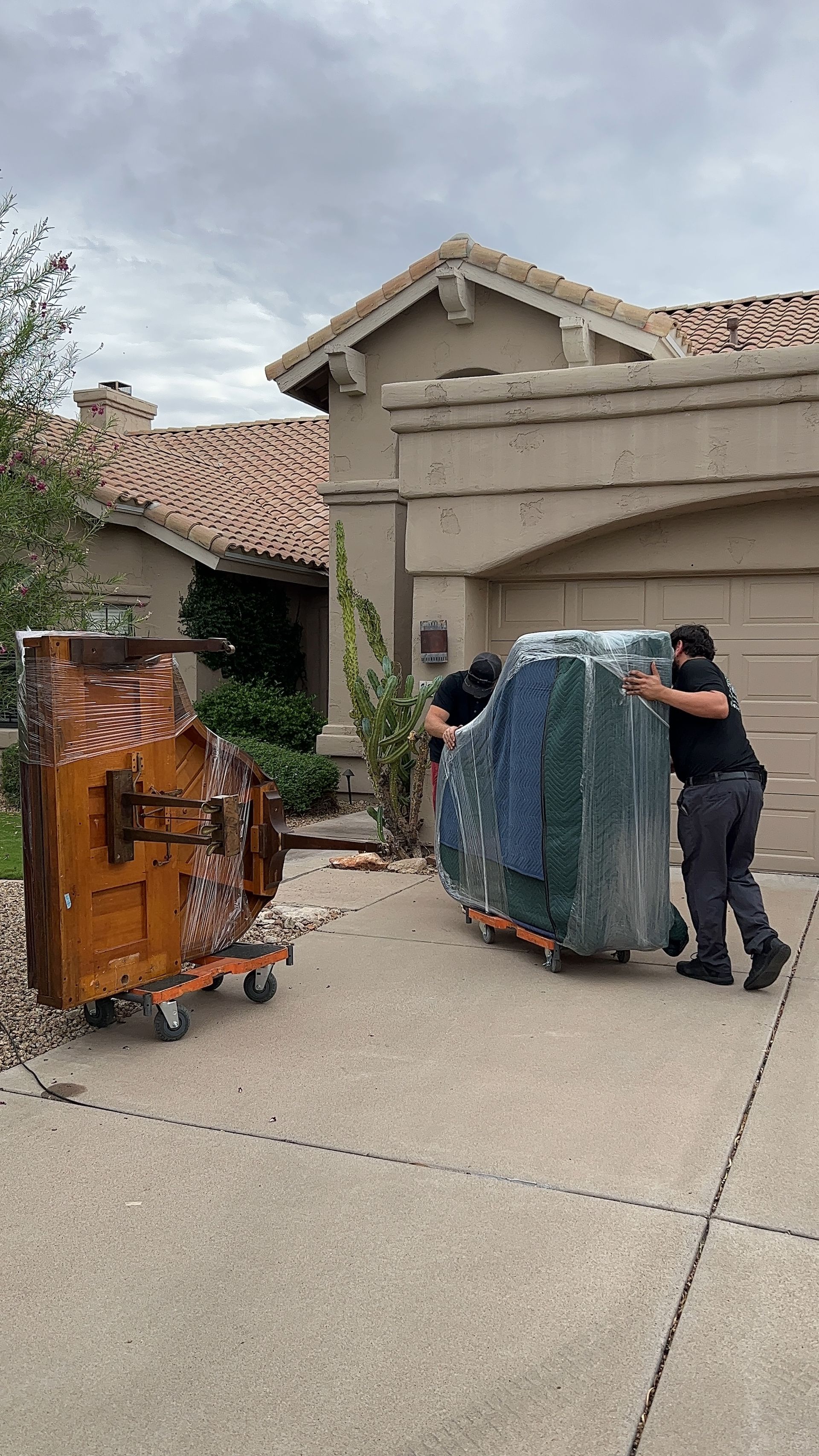 Two workers moving large furniture dollies on a driveway in front of a house