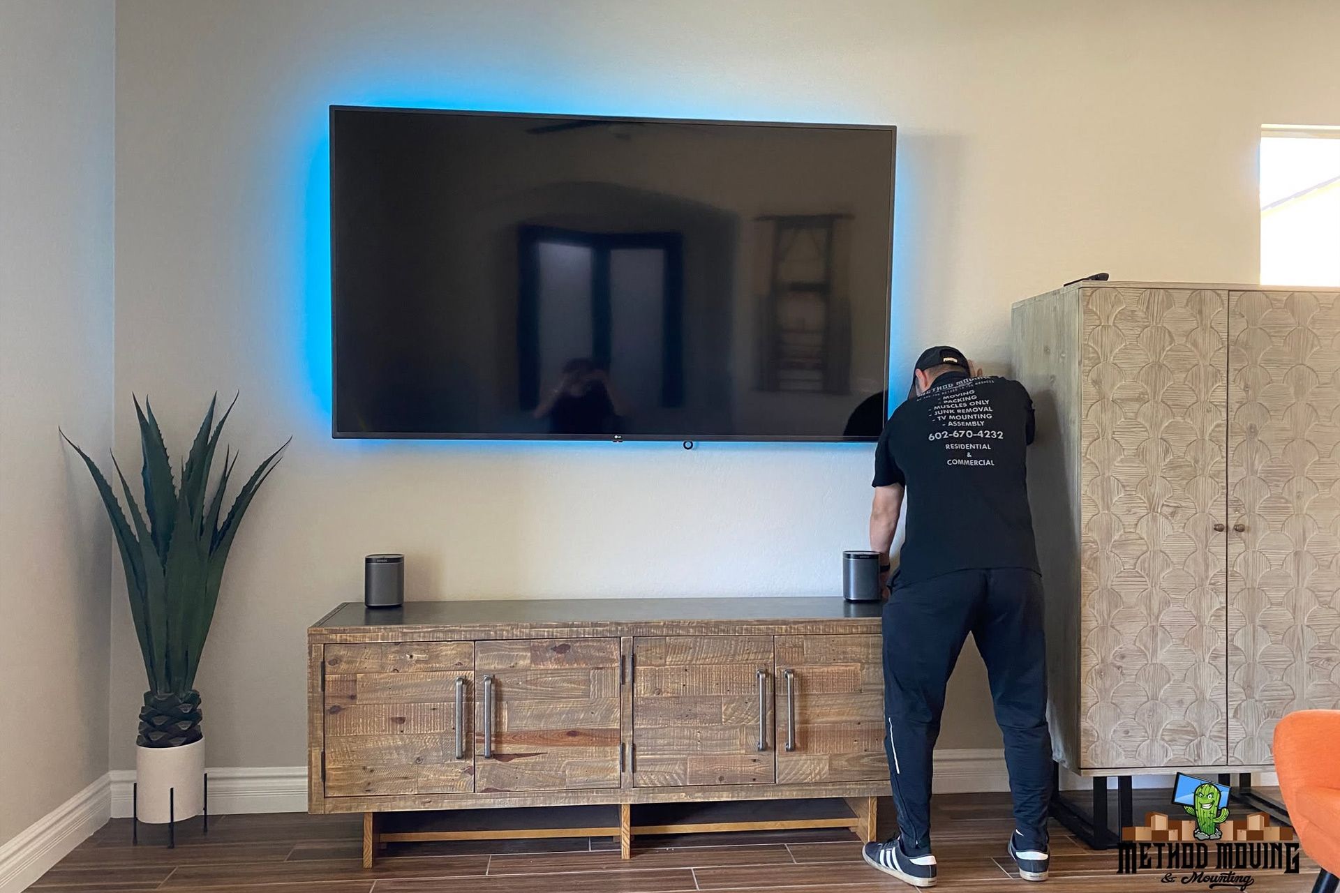 Person adjusting a wall-mounted TV in a living room with blue backlighting and a wooden console below