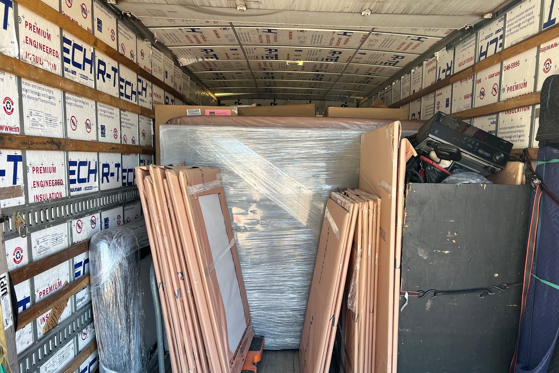 Box truck loaded with furniture and stacked wooden panels in a warehouse or moving setting