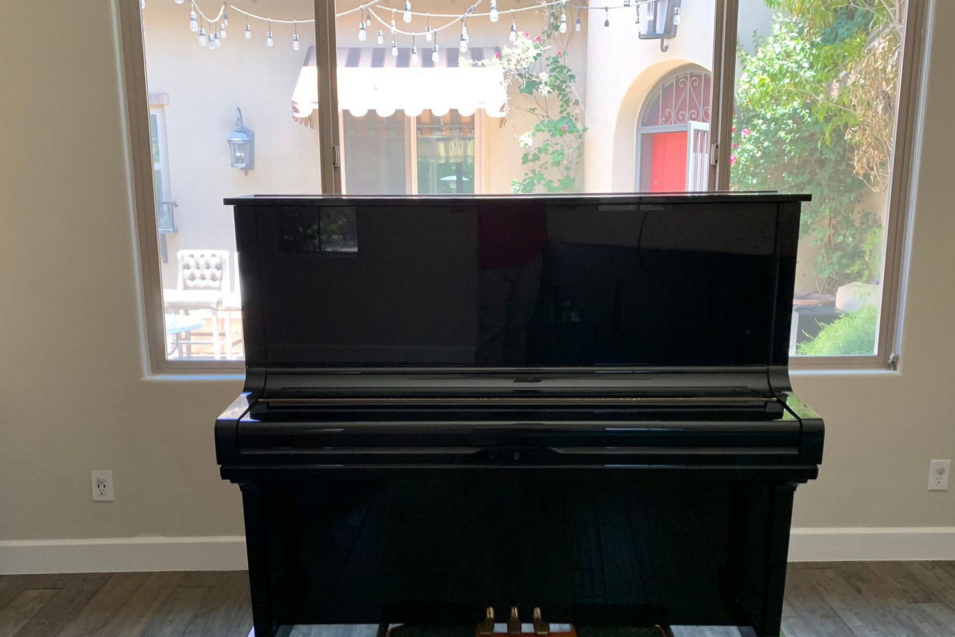 Black upright piano in front of a large window with a view of greenery and a patio