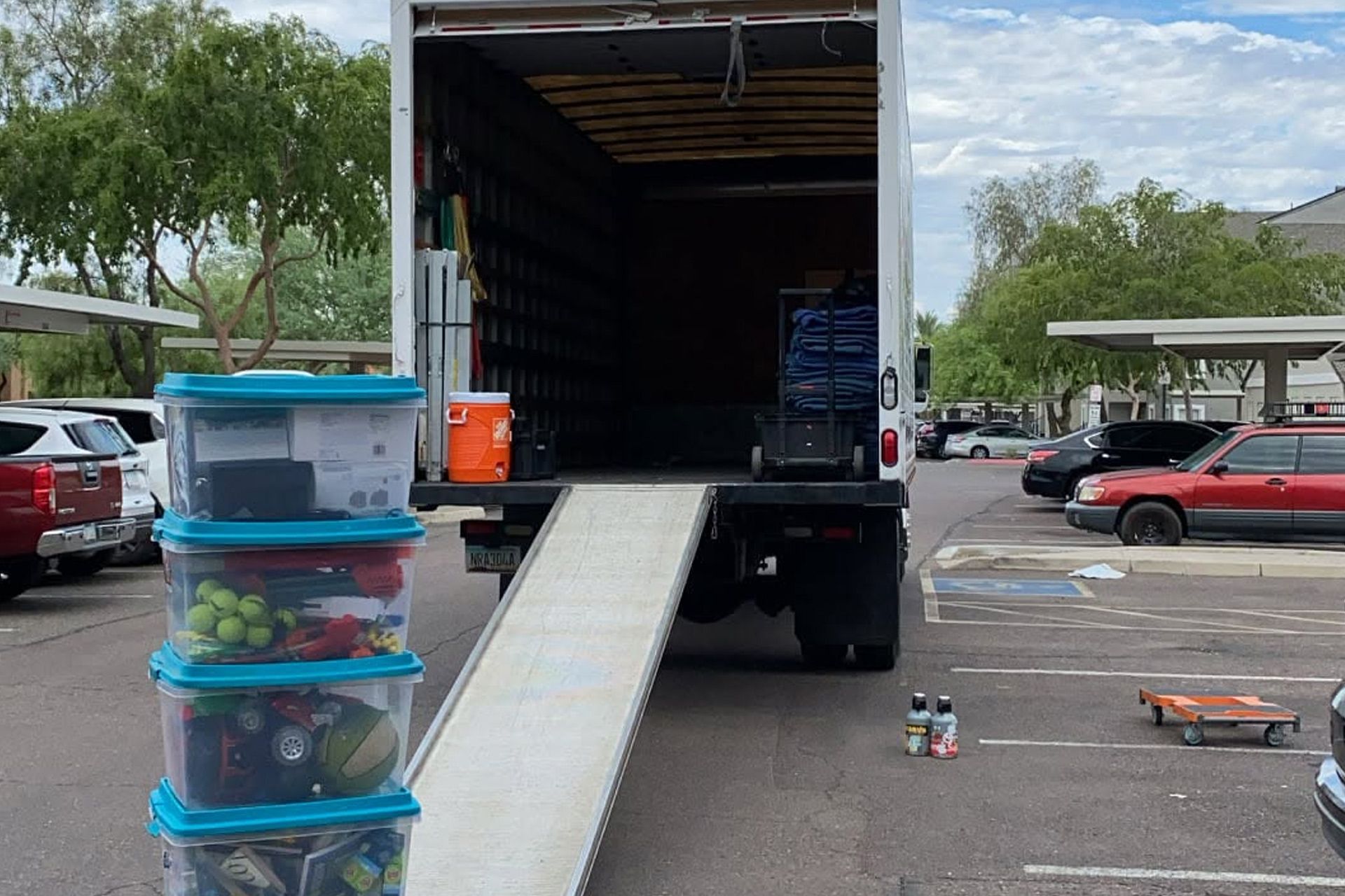 Truck with open cargo bay and ramp at a parking lot, with stacked storage bins in the foreground.