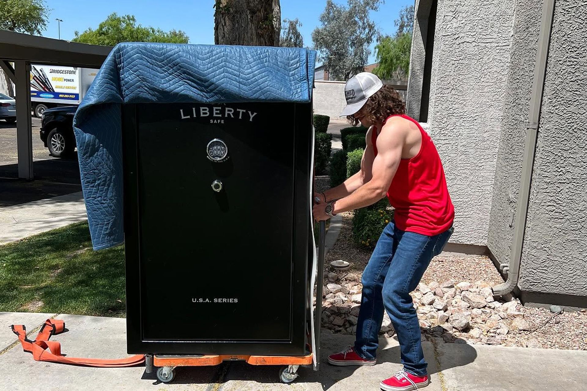 Person in red shirt moving a large black Liberty safe outdoors on a dolly.