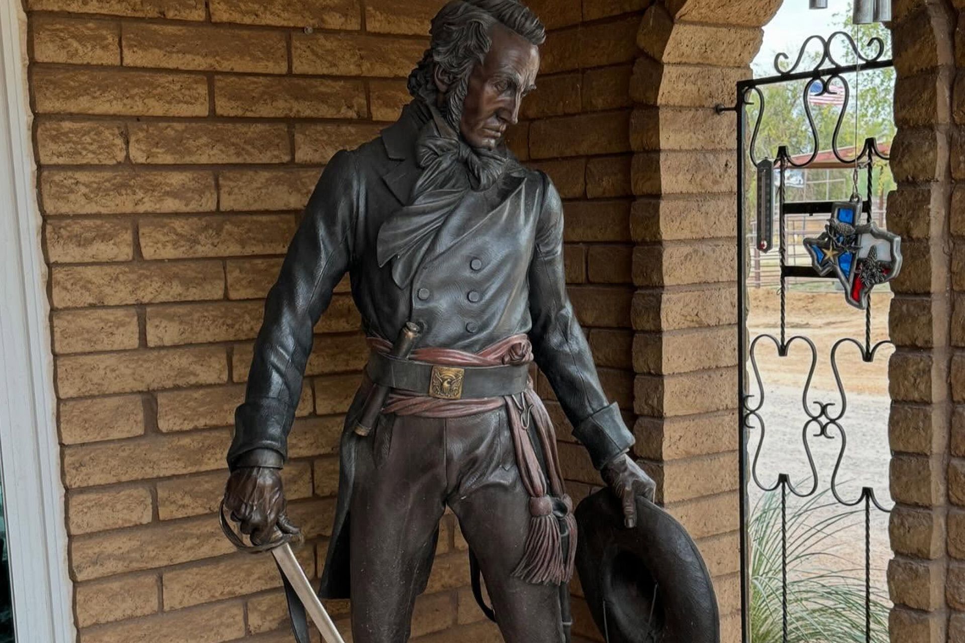 Bronze statue of a man in period clothing holding a hat, standing in a brick alcove.