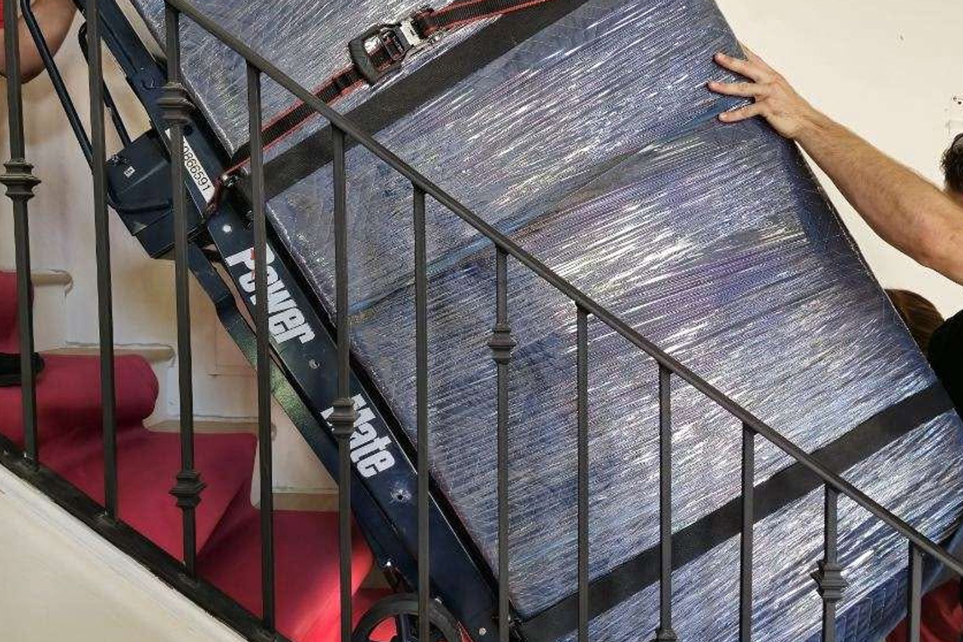 Person carrying a large framed panel up a staircase with a handrail.