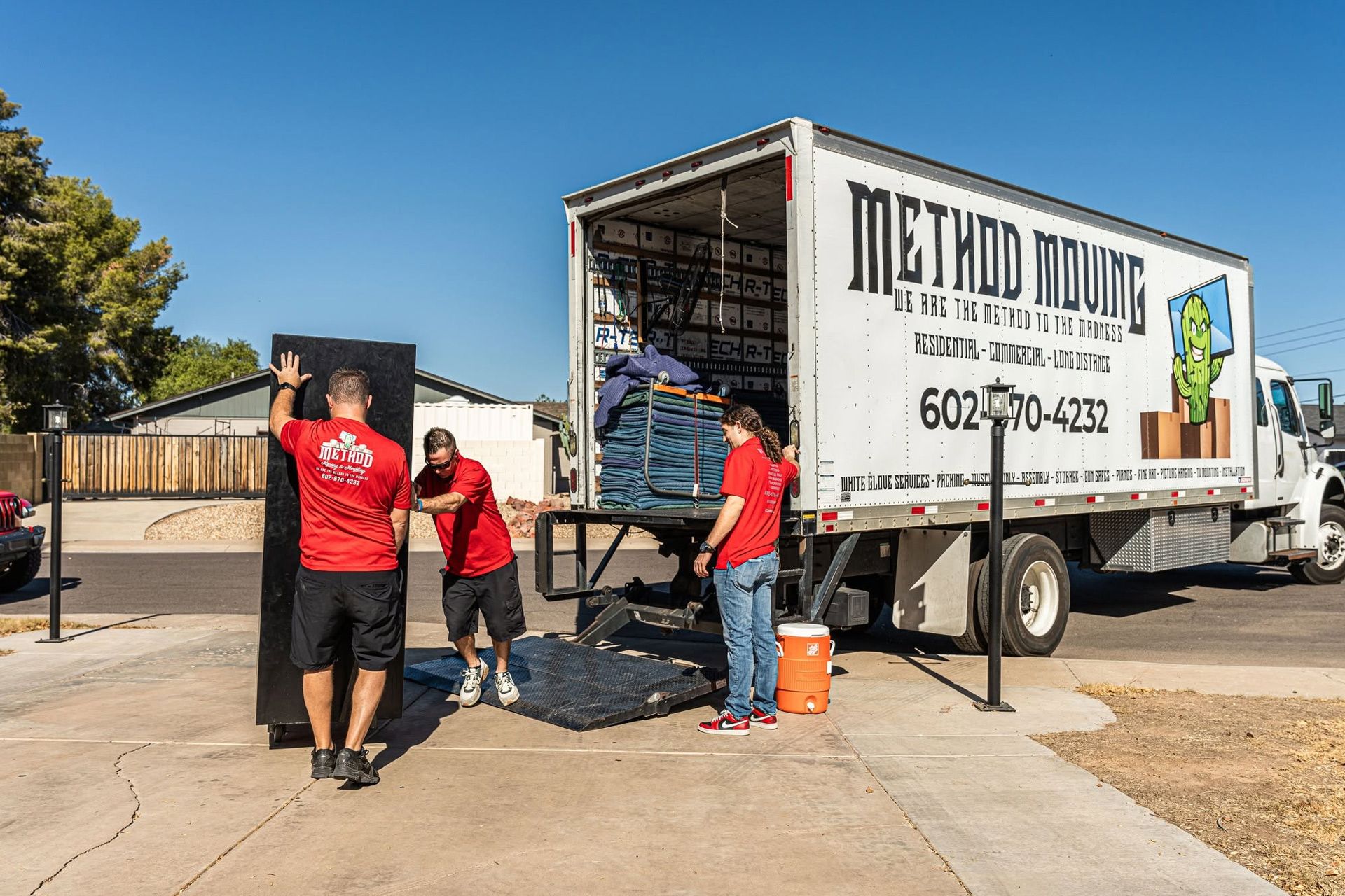 Movers loading furniture into a white truck at a sunny residential driveway