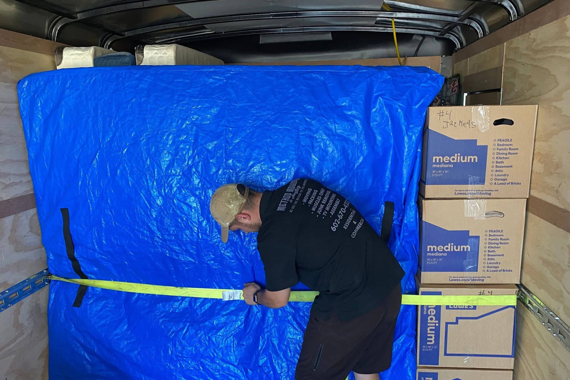 Person securing a large blue tarp over stacked boxes inside a moving truck.