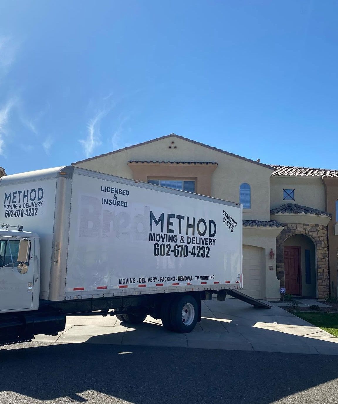 White moving truck with “METHOD Moving & Delivery” parked in front of a house on a sunny day