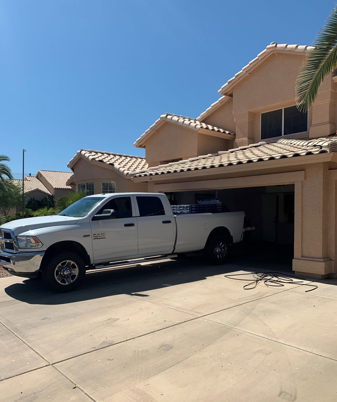 White pickup truck parked in a sunny driveway beside a tan two-story house