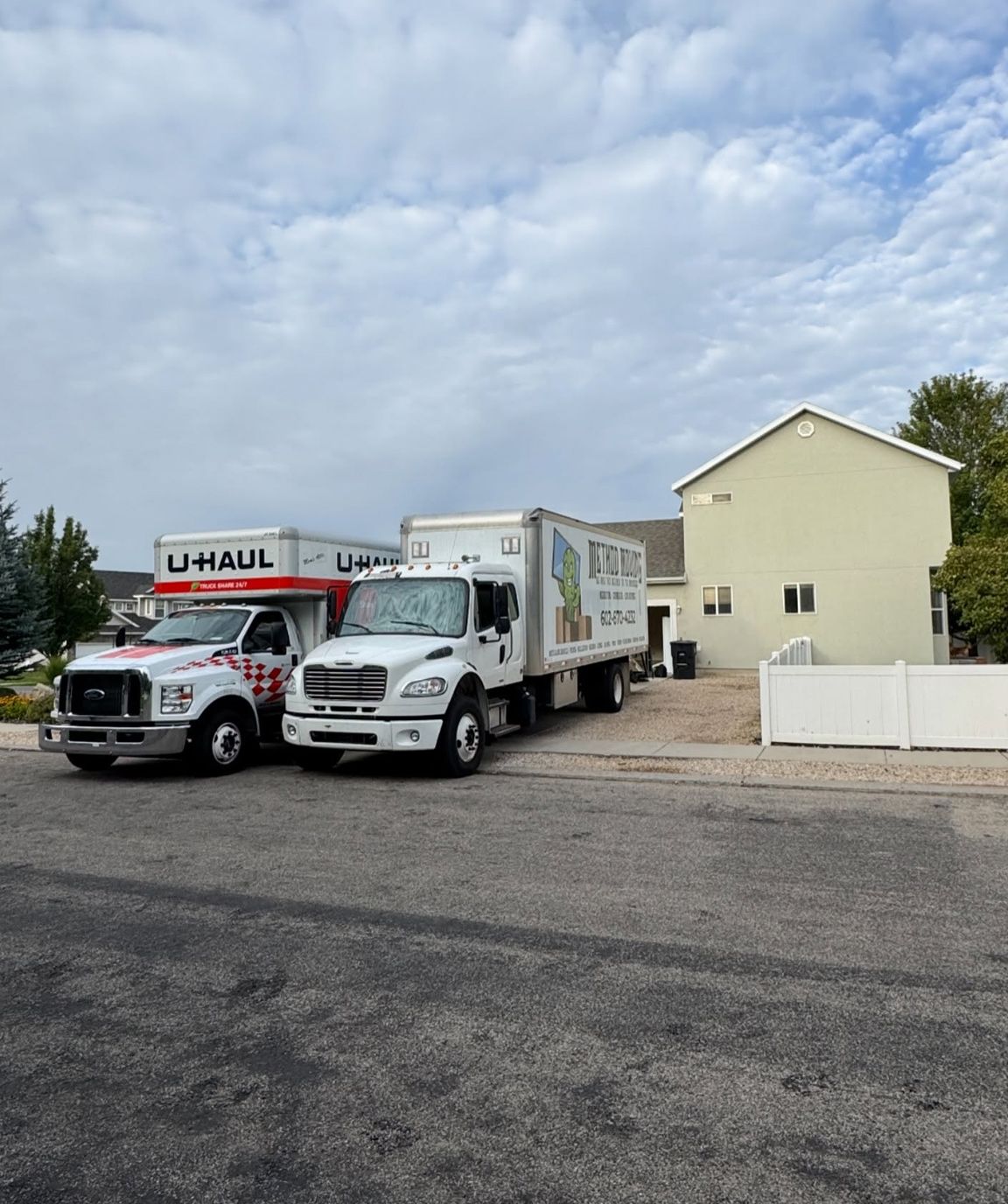 Two U-Haul trucks parked beside a beige house under a cloudy sky