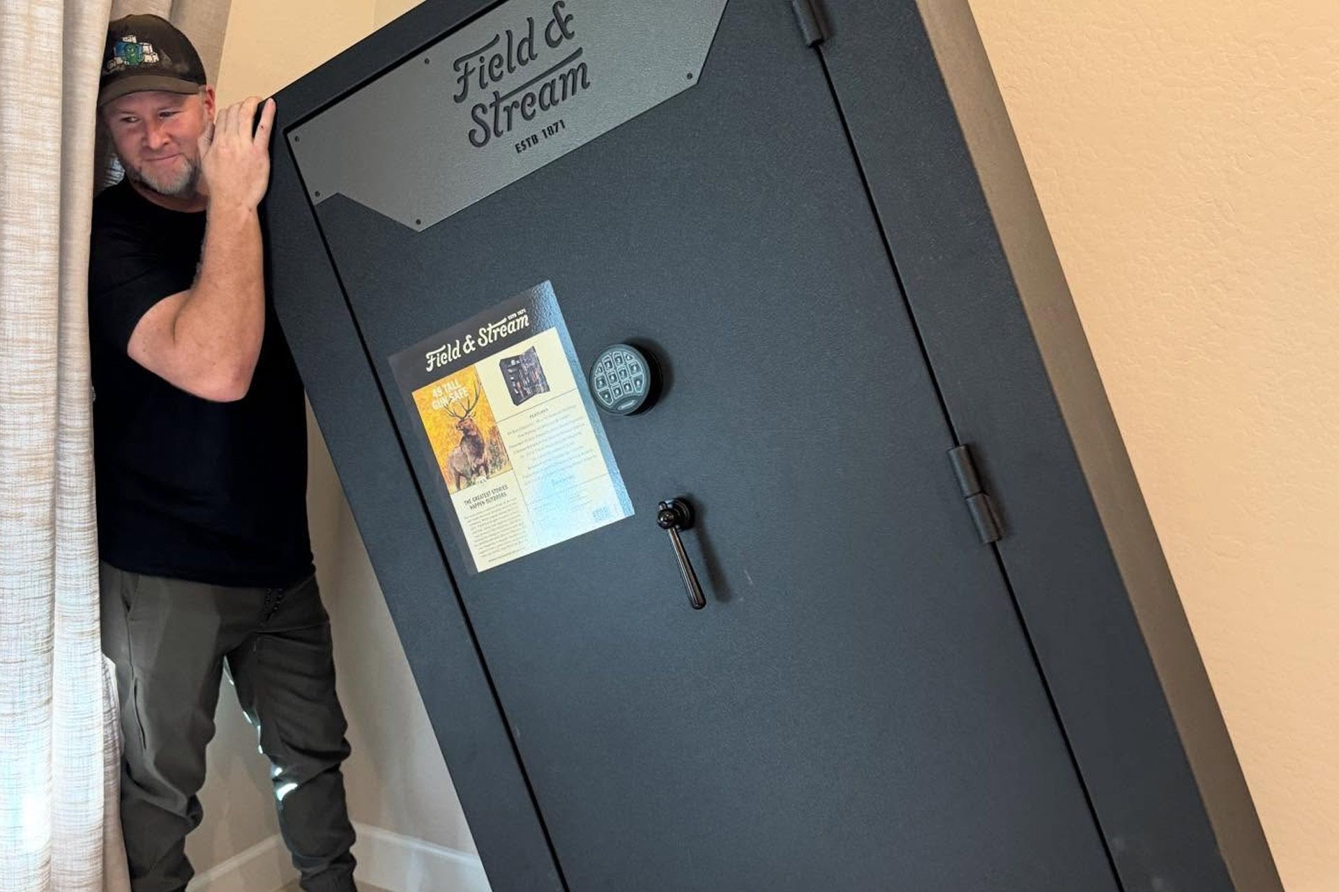 Man peeks from beside a large gray Field & Stream safe with a poster on the door.