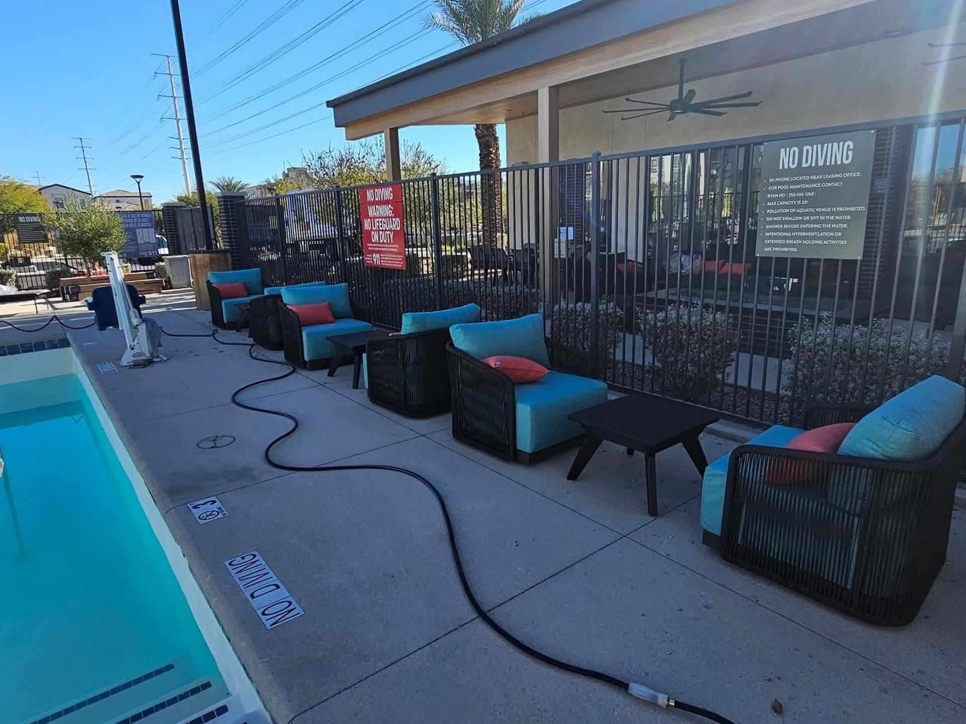 Outdoor patio seating with black chairs and turquoise cushions beside a fenced storefront