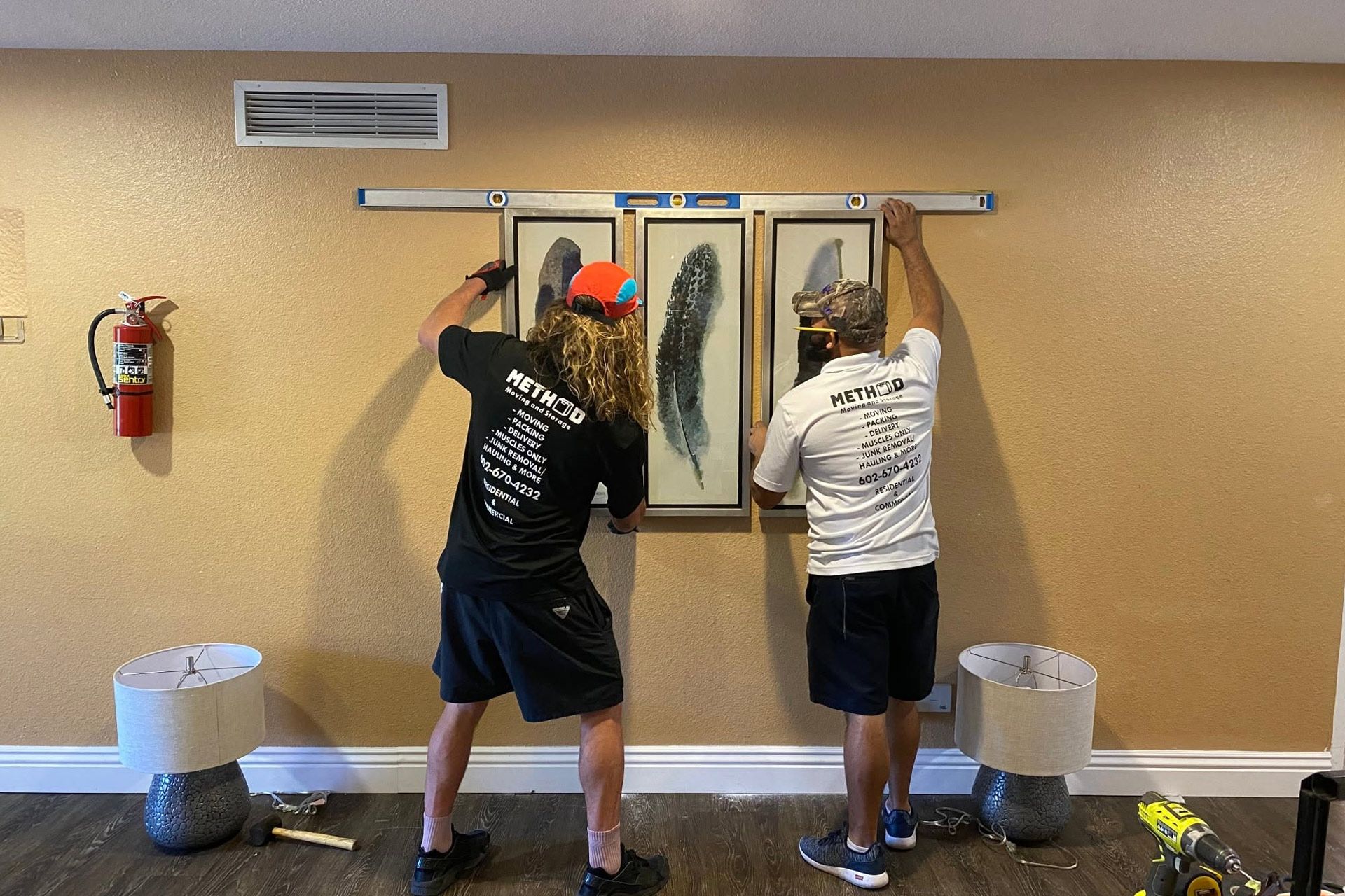 Two people hanging fish and gear on wall-mounted rods in a beige room with two buckets below.