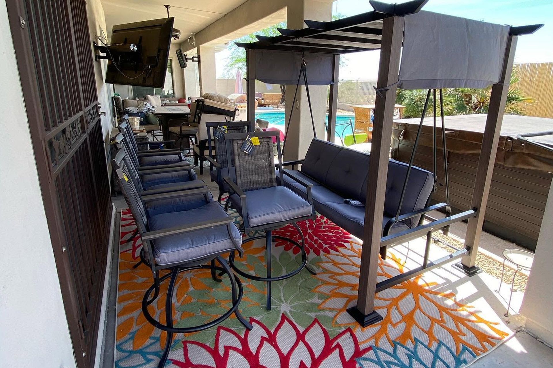 Covered patio with several cushioned lounge chairs, a swing bed, and colorful patterned rug.