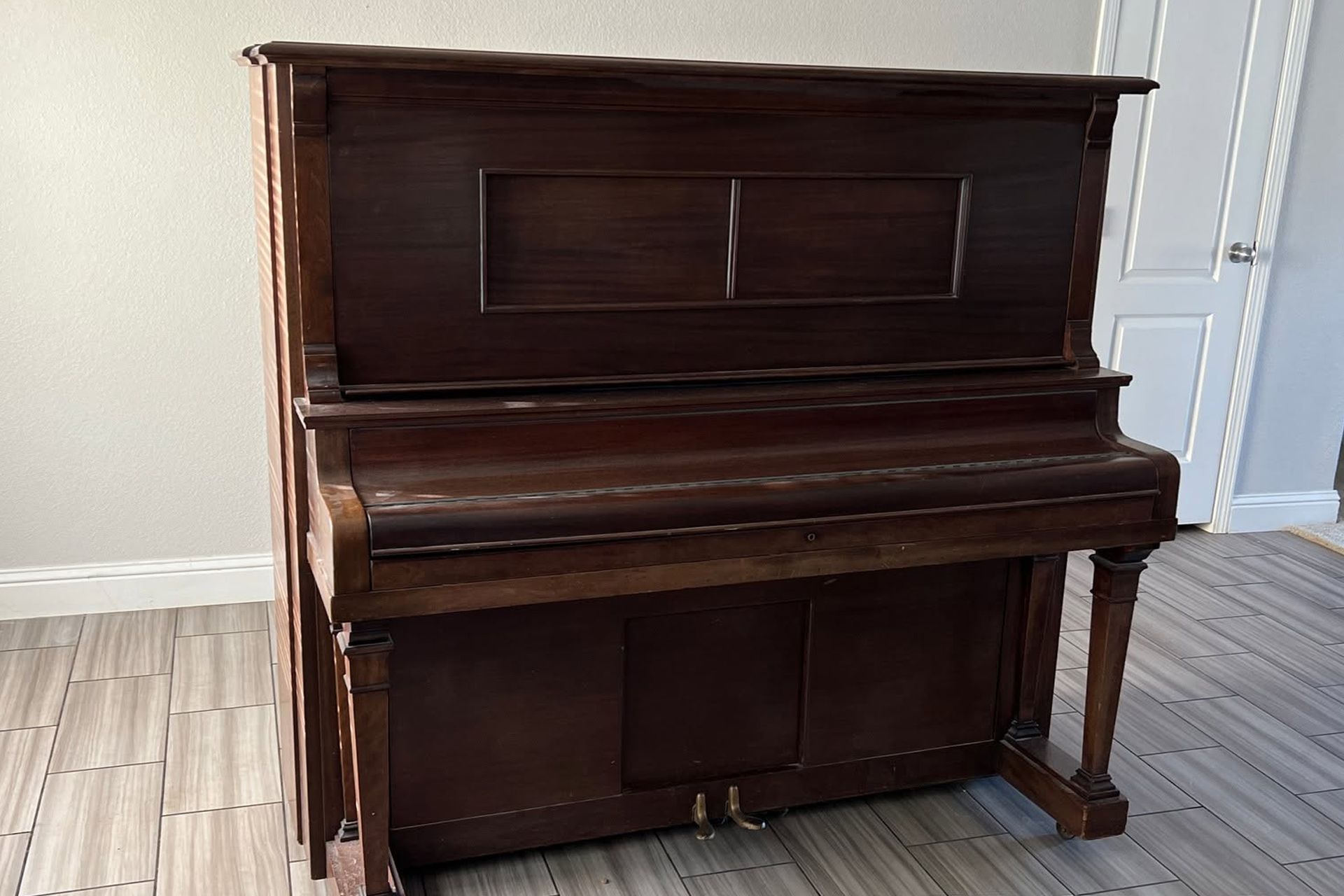 Dark wood upright piano against a wall on a light tiled floor