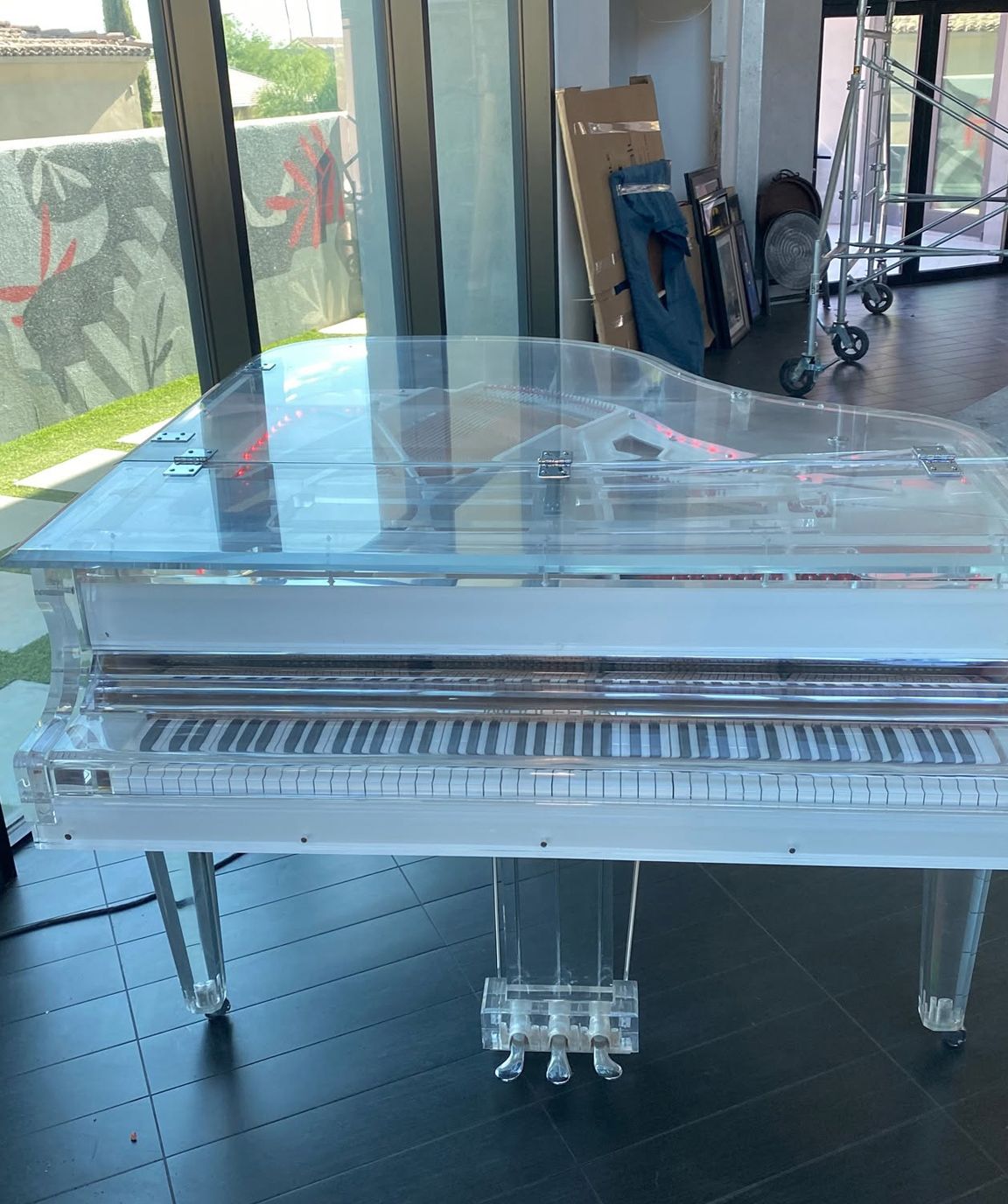 Clear acrylic grand piano on display in a room with dark tile floor and large windows